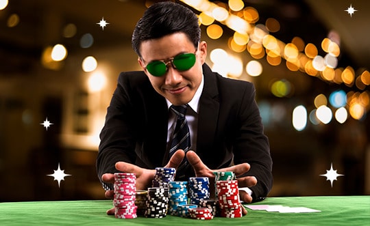 homem vestindo terno e óculos escuros em ambiente de cassino segurando fichas de poker em uma mesa de jogos